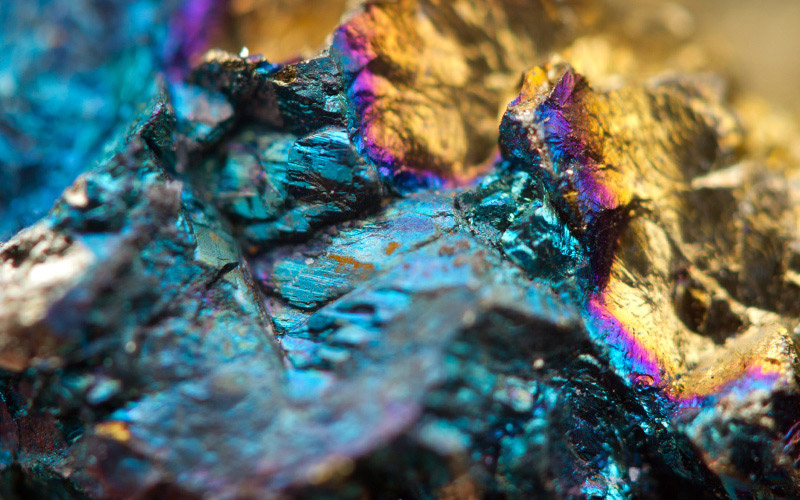 A close-up shows a rough mineral rock fragment displaying vibrant iridescent blue, purple, and gold colors