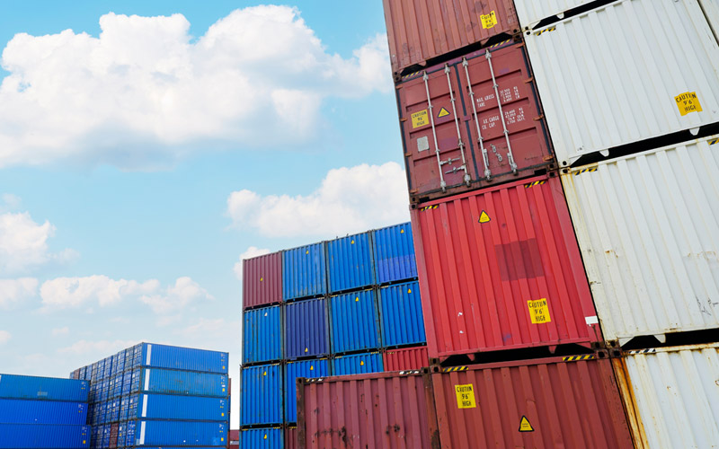 Stacked blue, white, and red shipping containers stand tall against a blue sky.